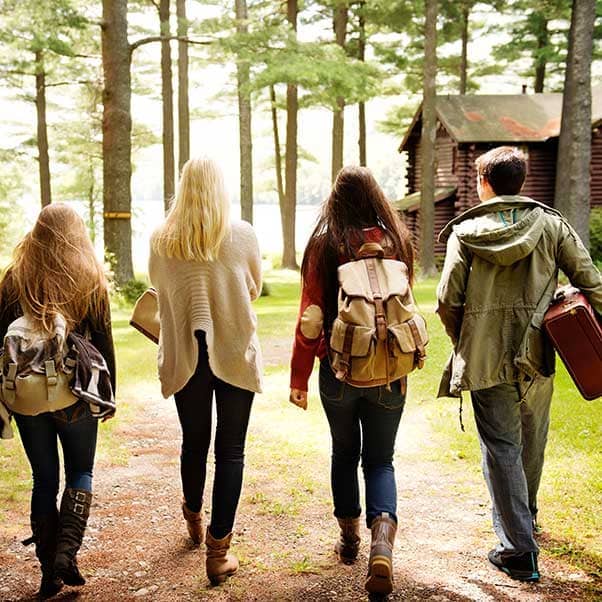Group of four students walking along a dirt track towards a wooden chalet and lake.
