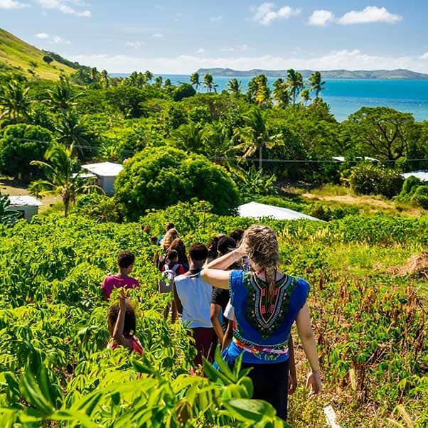 Volunteers walking though a field in Bali with the turquoise blue sea in the distance.