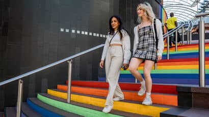 Two young women walking down a rainbow staircase.