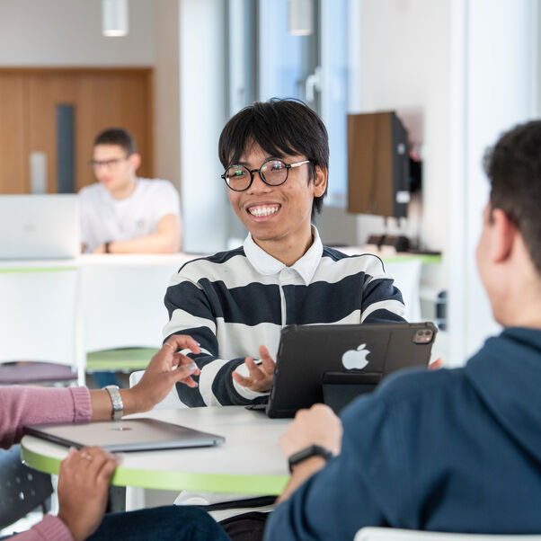 Student sat with a group around a table smiling with his tablet.