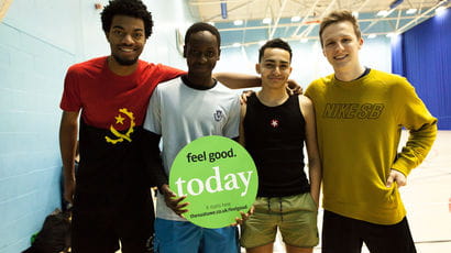 Four people in standing together facing front, one with an arm around the others
