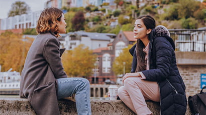 Two students sitting on a wall by the harbourside talking to each other.