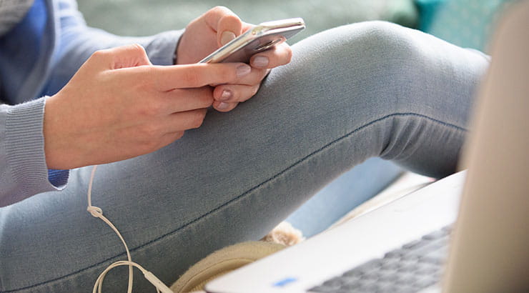 Hands holding phone, laptop in the foreground
