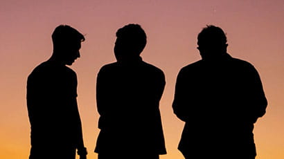 Image of three male figures talking in silhouette against a sunset.
