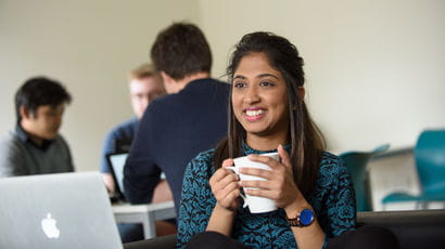 A student holding a coffee cup and smiling