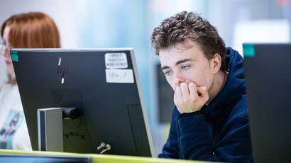 Student resting on elbow looking at a pc.