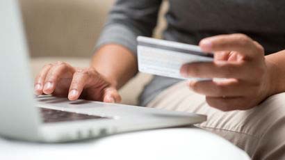 Close up of someone entering details into a laptop holding a cash card.