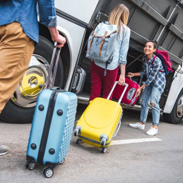 Smiling woman loading her suitcase into the luggage compartment of a white coach