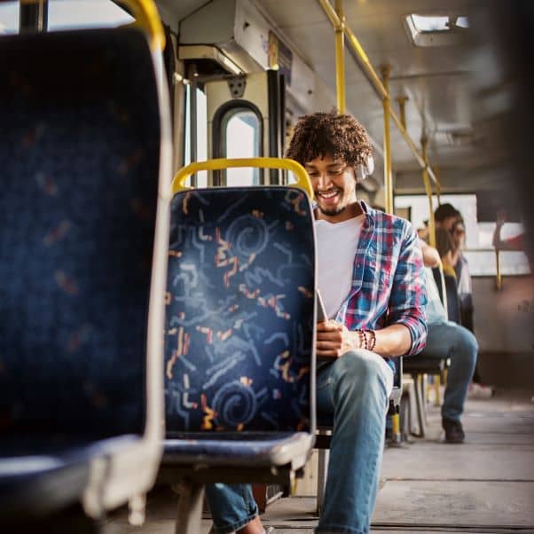 Smiling man sitting on a bus listening to music on headphones