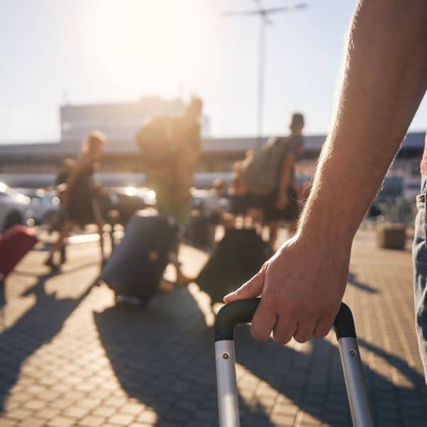 Close up of an arm pulling a suitcase towards cars outside an airport terminal