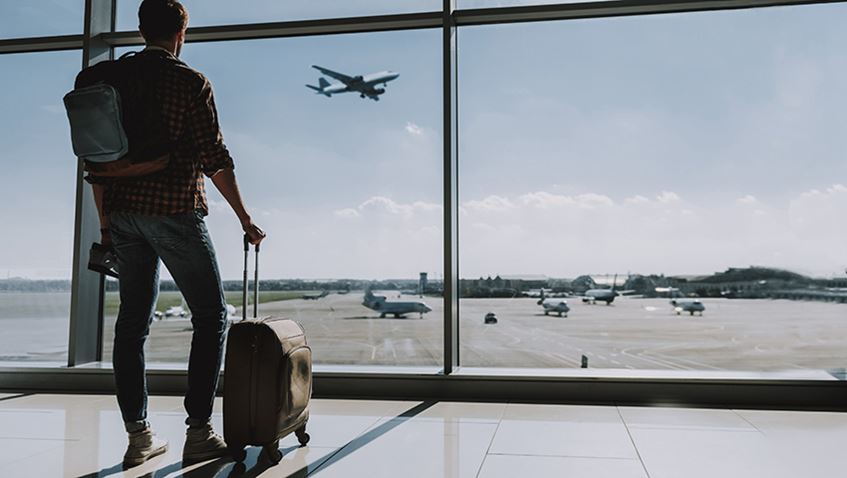 A man with a suitcase standing in an airport terminal watching planes take off