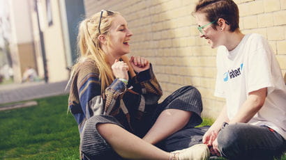 Two students laughing together whilst sat outside of their accommodation