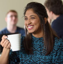 A student smiling and holding a cup of tea