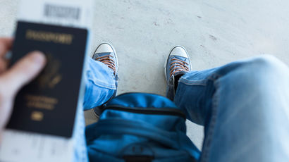 A close up of a passport, a backpack and feet in trainers