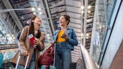 Two young people with suitcases laughing and chatting in an airport terminal