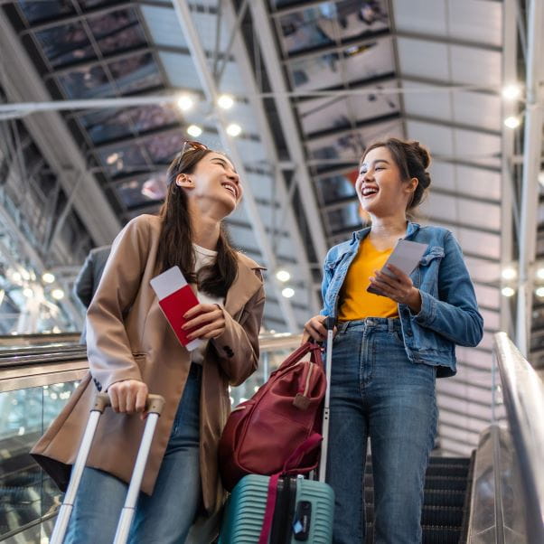 Two young women smiling and chatting at an airport terminal