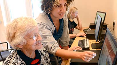 A volunteer helping an elderly woman to use a computer.