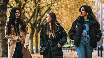 Three students walking together in Bristol with trees covered in yellow autumn leaves in the background.