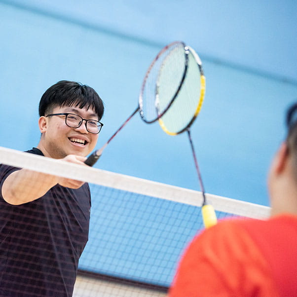 A student touches badminton racket with his competitor over the net.