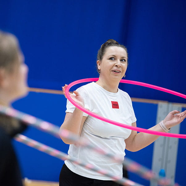 A woman in sports clothing smiles to a friend while balancing her hula hoop around her neck.