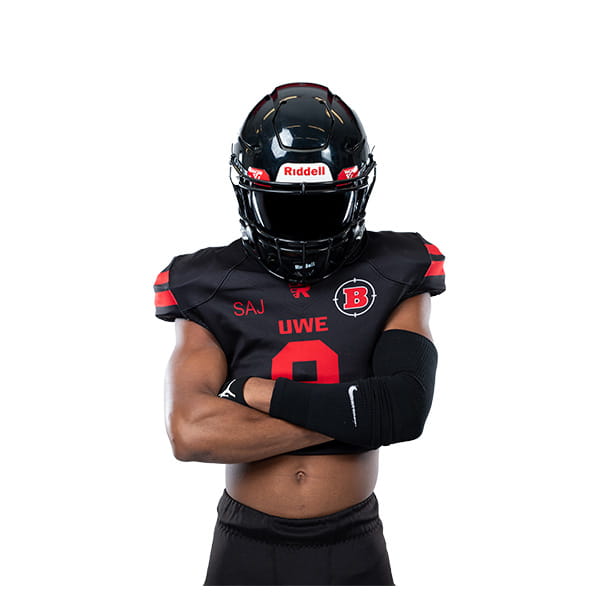 American Football player with helmet visor down, arms crossed.