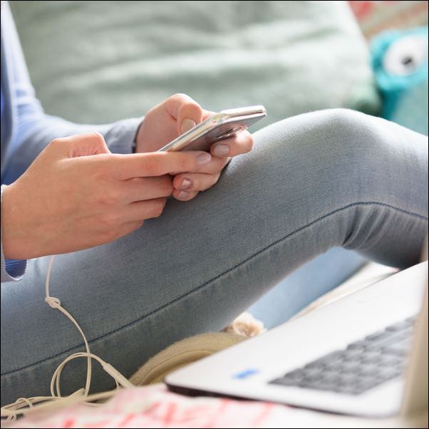 Closeup of someone using a phone while using a laptop.