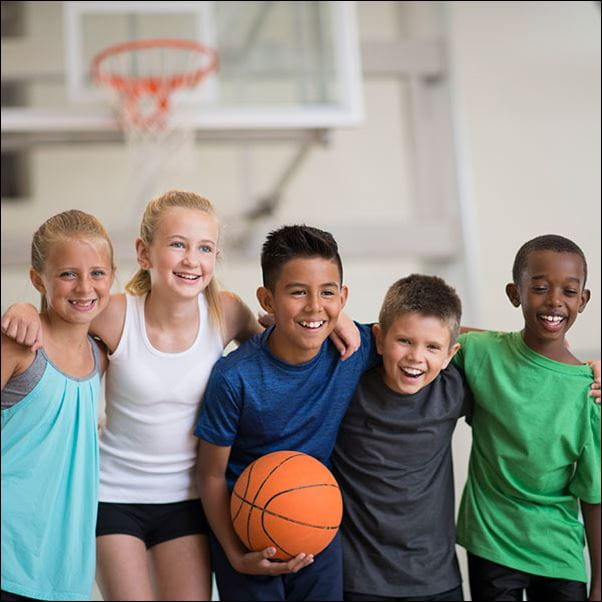 Children dressed in sports clothing posing with a basketball.