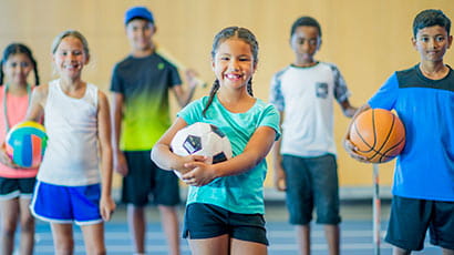 Children dressed in sportswear holding footballs.