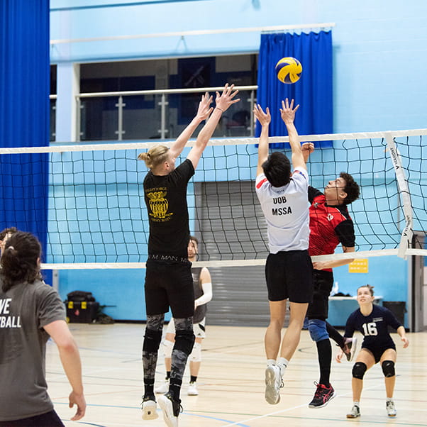 Two volleyball players jump to block the ball during a match in the Sports Hall at UWE Bristol Centre for Sport. 