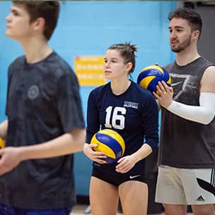 Three competitors holding volleyballs on a volleyball court.