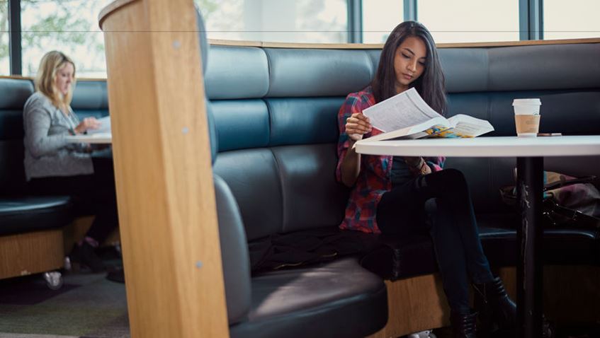 Female student with a coffee in the seating area of the SU