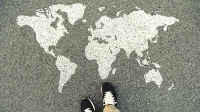 World map on an asphalt road. Top view of the legs and shoes of someone standing next to it.