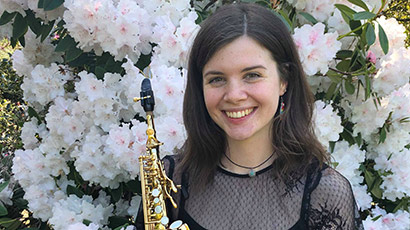 Portrait of Chloe Buttery standing in front of a flowering shrub. Portrait of Chloe Buttery standing in front of a flowering shrub.