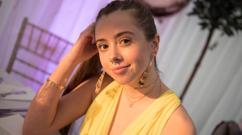 Young woman, Ellie in yellow top looking at camera with head leaning on her hand