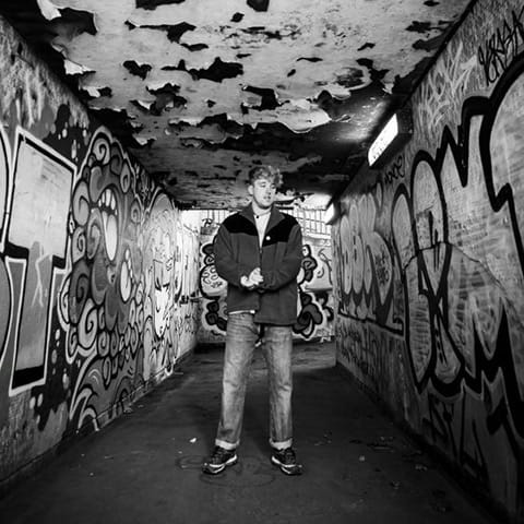 James Tombling short in black and white in front of graffitti.