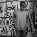 James Tombling short in black and white standing in front of graffitti.