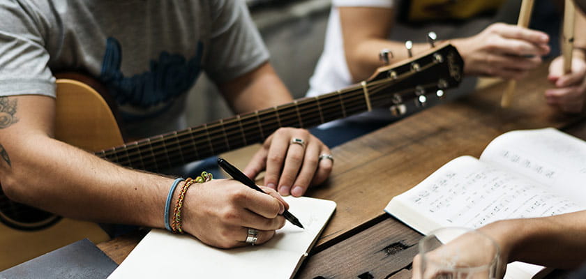 Closeup of a group of people writing a song using a guitar.