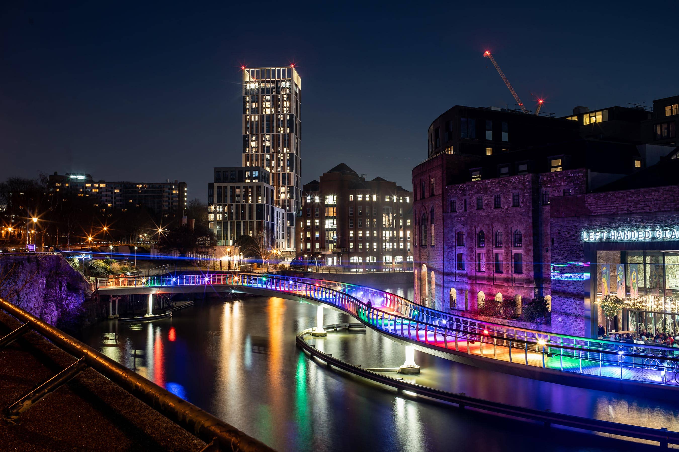 Bristol harbour at night with led lights shining on the bridge.