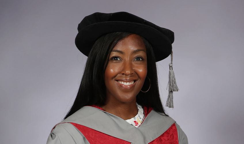 A lady smiles at the camera wearing a graduation cap and gown