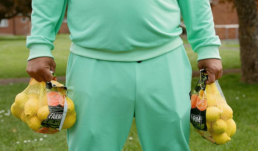 A man wearing a green tracksuit holds a bunch of bananas in each hand. 