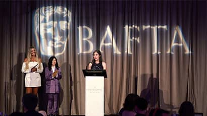 A woman stands at a lectern making an acceptance speech for an award, with the BAFTA logo behind her.  