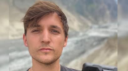 A man stands in dramatic landscape looking at the camera