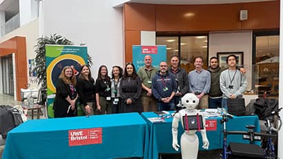 UWE Bristol staff and partners stand behind an information table alongside a humanoid robot and mobility equipment at a community engagement event.