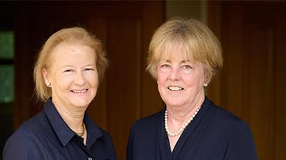 A headshot of two women smiling against a brown background