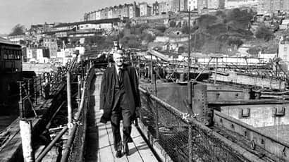 Hollywood star Cary Grant smiles at the camera as he walks over a bridge in Bristol