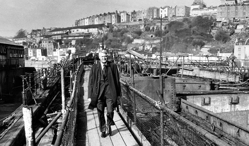 A black and white photo of Hollywood star Cary Grant who smiles at the camera whilst walking across a bridge at Bristol Harbour.