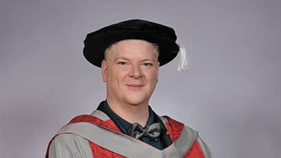 A headshot of a man wearing a graduation cap and gown 