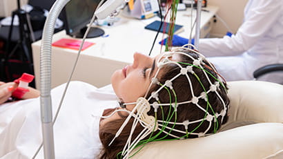 A woman is lying down in a hospital with a series of wires covering her head to monitor brain activity.