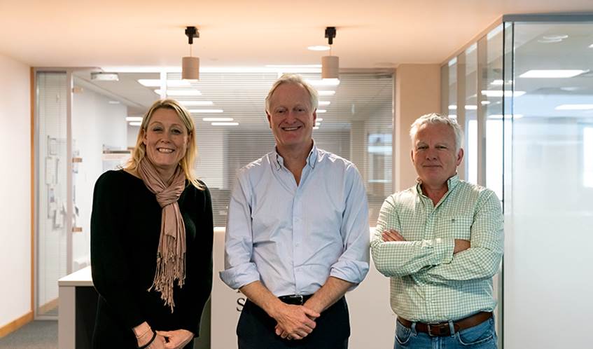 A woman and two men stand in line smiling at the camera in an office building
