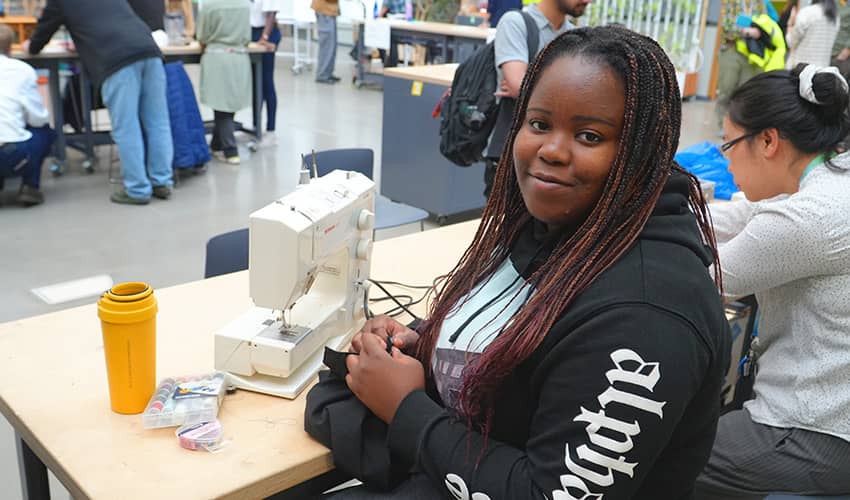 A woman sits in front of a sewing machine looking at the camera. 